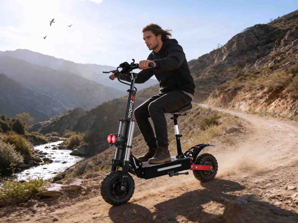 Person riding a ZO03 5600W electric scooter on a dirt trail with mountains in the background